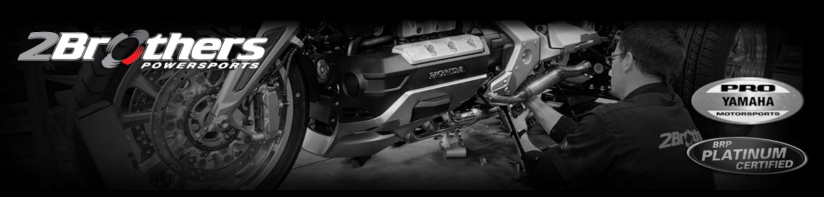 A person working on an exhaust on a motorcycle parked inside a shop near a tire.